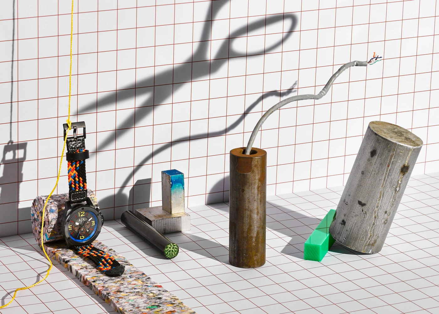 Still life still featuring a wristwatch with a patterned band, metal cylinders, and a scissors shadow on grid paper.