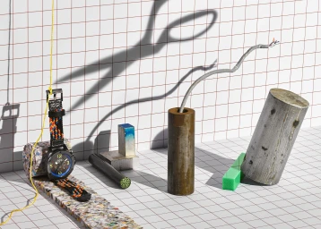 Still life still featuring a wristwatch with a patterned band, metal cylinders, and a scissors shadow on grid paper.