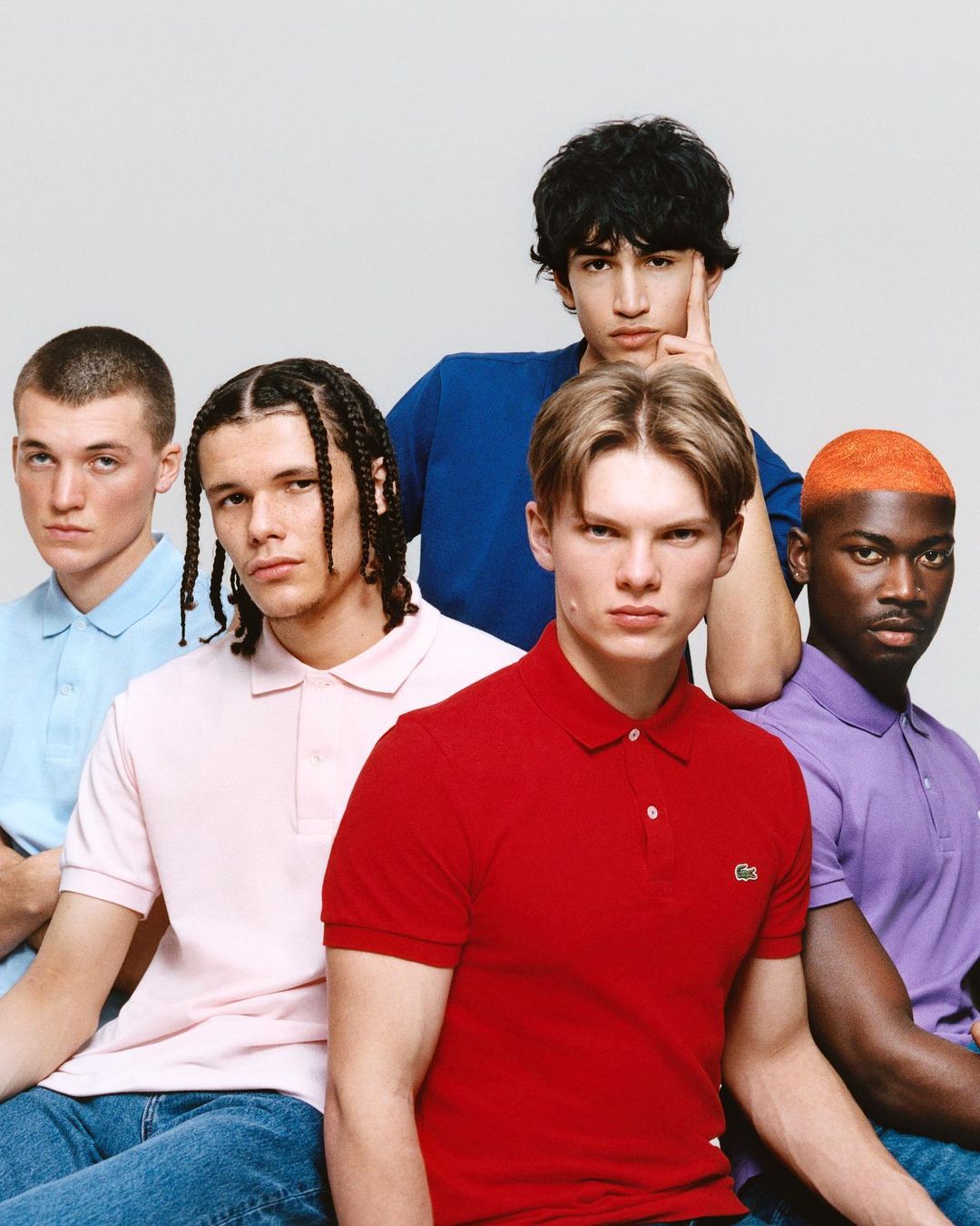 Group portrait of five young men in blue jeans wearing various colored polo shirts in front of a white background in a studio.