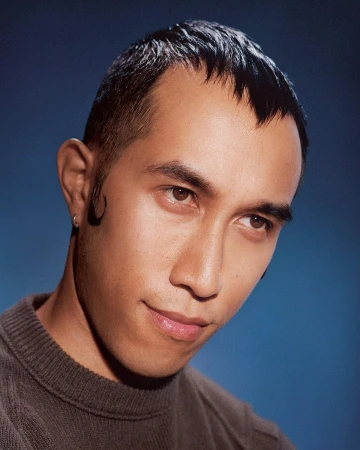 Portrait of an Asian man with short dark hair and a small earring against a blue background