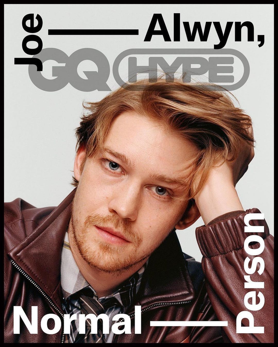 Close-up portrait of Joe Alwyn on a magazine cover, wearing a brown leather jacket, grey background with magazine text and logos.