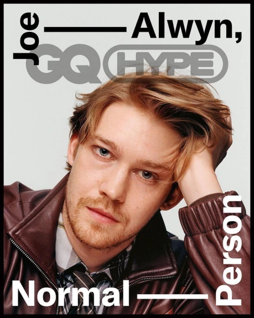Close-up portrait of Joe Alwyn on a magazine cover, wearing a brown leather jacket, grey background with magazine text and logos.