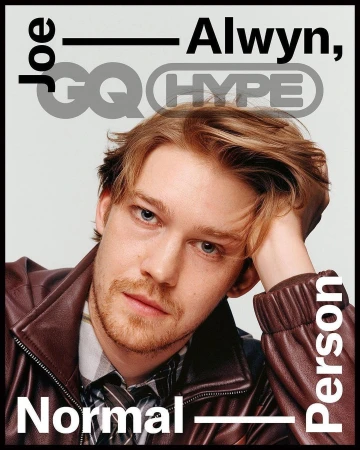 Close-up portrait of Joe Alwyn on a magazine cover, wearing a brown leather jacket, grey background with magazine text and logos.