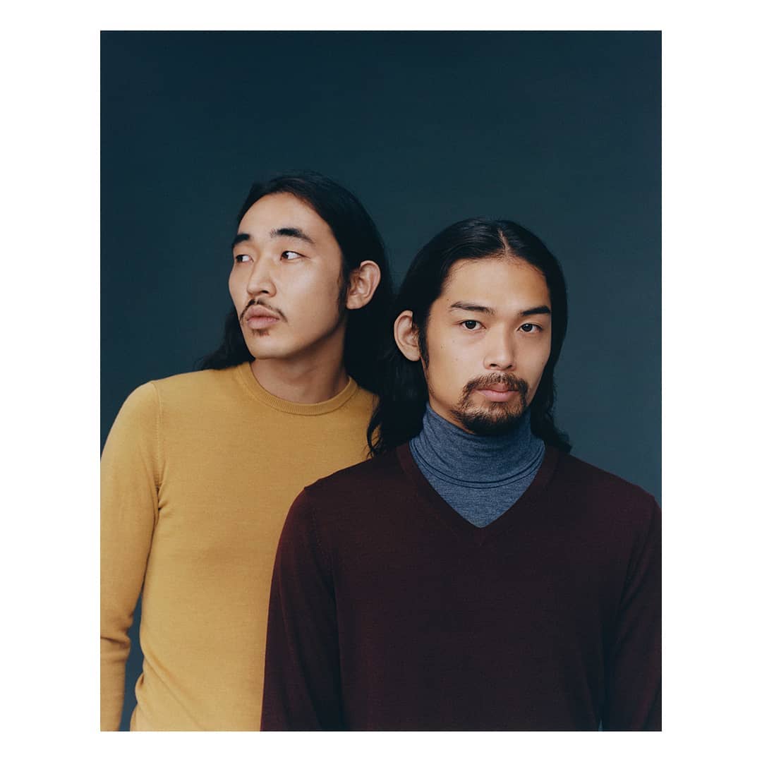 Two Asian men in a studio portrait. One is in mustard yellow, looking left; the other in burgundy with a gray turtleneck, looking forward.