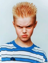 Young person with spiky blonde hair and scowling expression wearing a blue and white striped t shirt against a light grey background