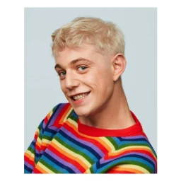Close-up portrait of a young man with blonde hair wearing a colourful striped sweater against a pale blue background