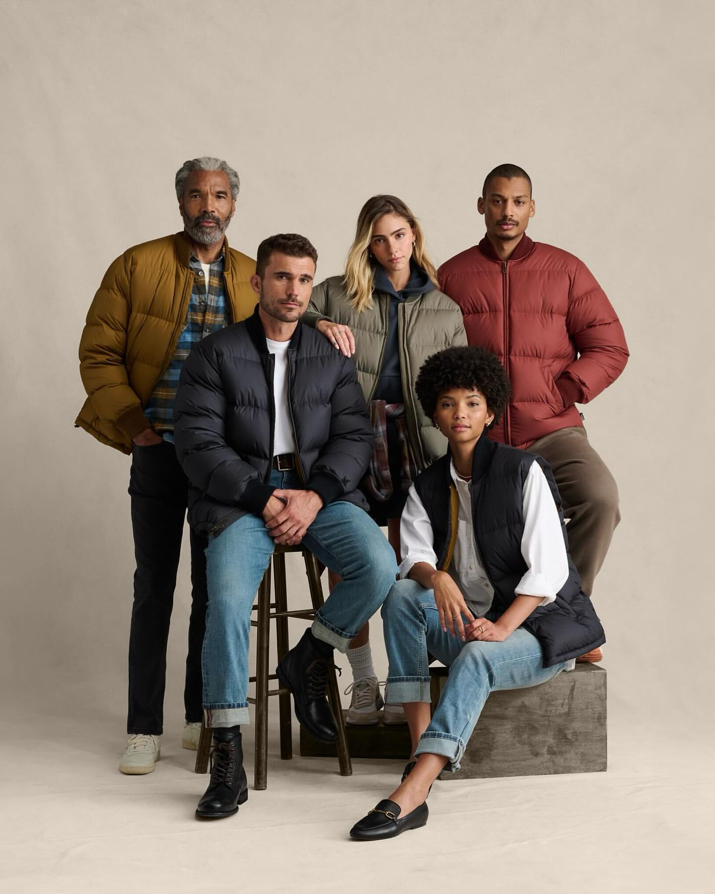 Group of five diverse adults wearing puffer jackets and vests in a studio shot, modelling an apparel collection.