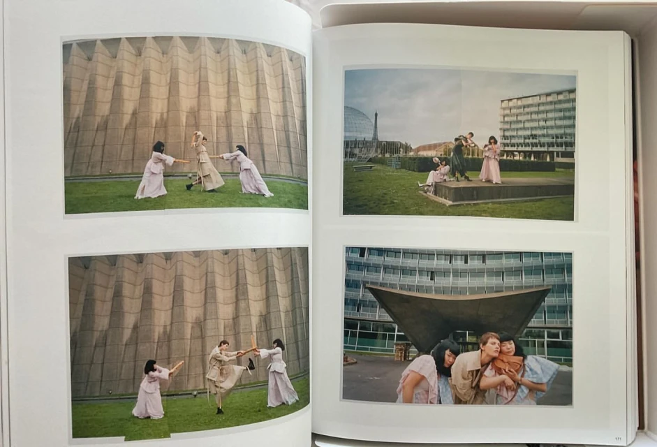 Open book featuring fashion photography: groups of women in flowing dresses interact outdoors in an editorial style against modern architecture.