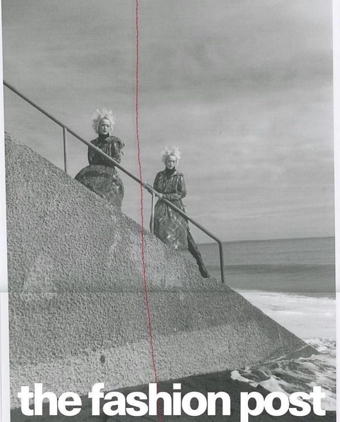 Two women with spiked hair pose on a concrete structure near the ocean in a black-and-white fashion shot for 'The Fashion Post'.