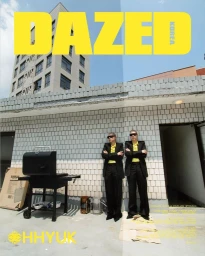 Two people wearing black suits and yellow shirts standing with arms crossed on a rooftop by a grill.