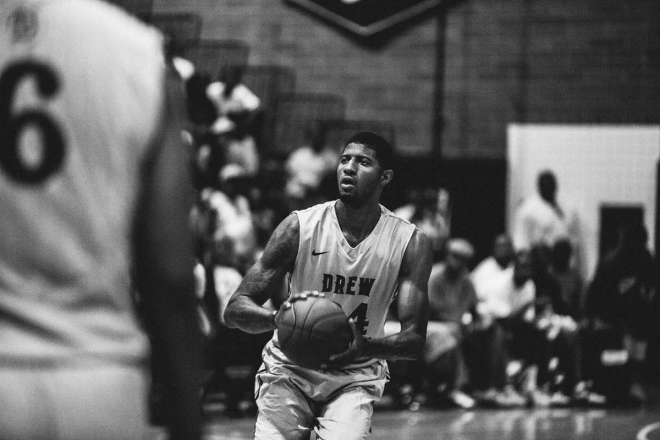 Monochromatic action shot of a basketball player in a jersey, holding a basketball during a game, with spectators in the background.