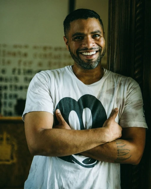 Smiling man with arms crossed wearing a t-shirt with a large Mickey Mouse graphic, posing indoors with fair skin, in a medium shot.