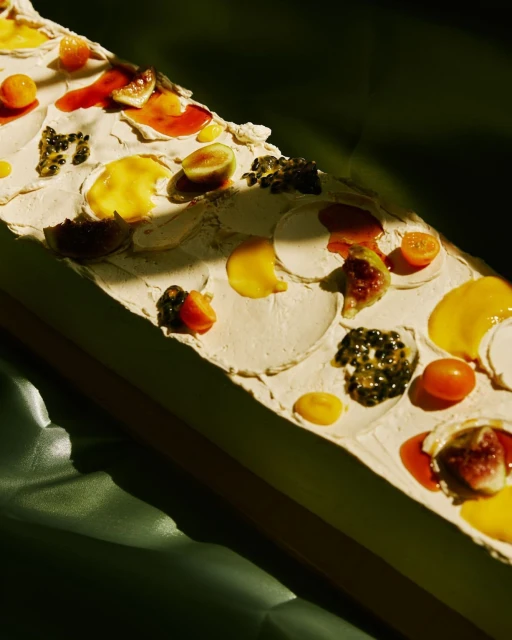 Overhead shot of an abstract food art composition featuring a creamy white base with figs, passion fruit, kumquats and red and yellow sauces.