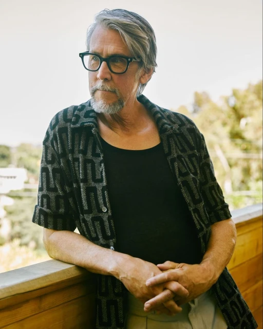 Portrait of a mature adult male with gray hair and glasses wearing patterned shirt, posing outdoors on a sunny day. 