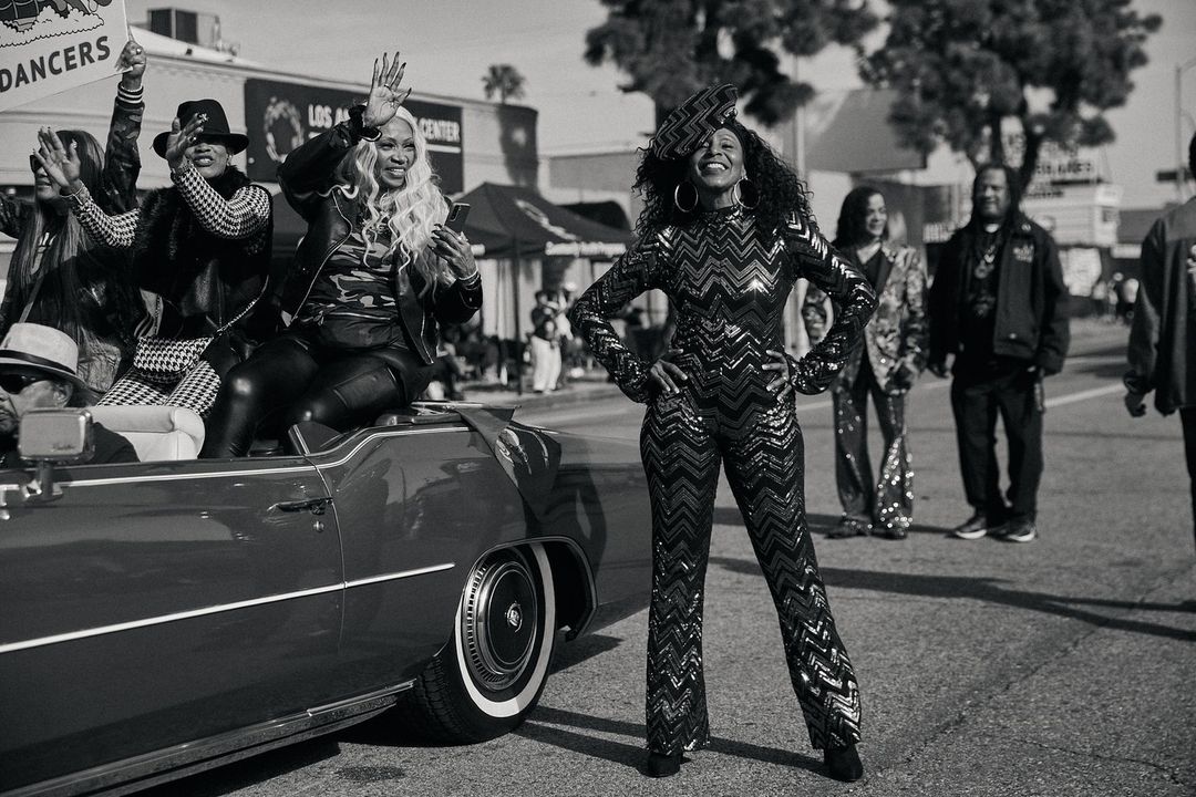 Black and white street photograph of a woman posing in a chevron patterned jumpsuit beside a convertible car in Los Angeles.