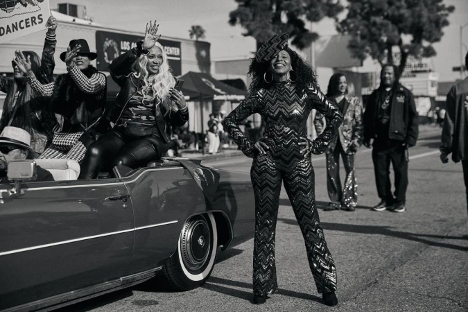 Black and white street photograph of a woman posing in a chevron patterned jumpsuit beside a convertible car in Los Angeles.
