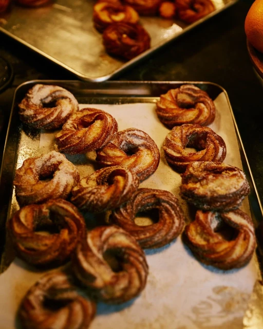 Several trays of freshly baked kouign-amann pastries with a golden-brown color, some dusted with sugar, arranged indoors.