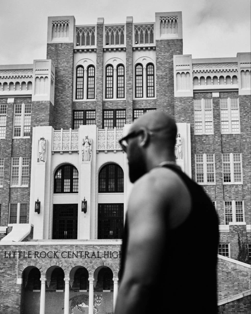 Black and white portrait of a bald man in front of Little Rock Central High School, Arkansas, featuring historic architecture.