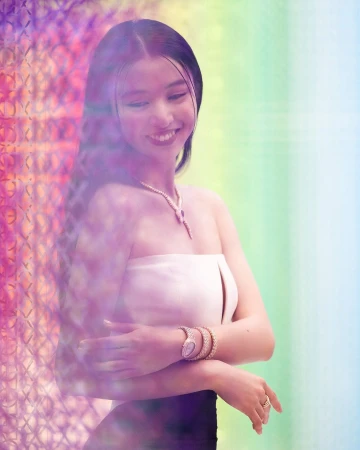 Smiling woman wearing a white strapless top, diamond necklace, and bracelets against a colorful gradient backdrop.