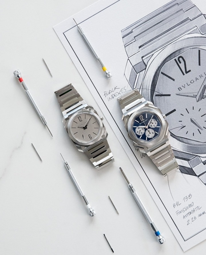 Two Bulgari watches are showcased alongside a detailed sketch and watch-repair tools on a white surface in this product shot.