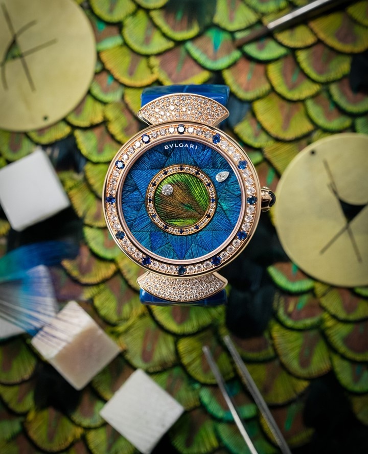 Elegant Bulgari watch featuring a peacock feather dial, surrounded by diamonds and sapphires, laying on a bed of vibrant peacock feathers.