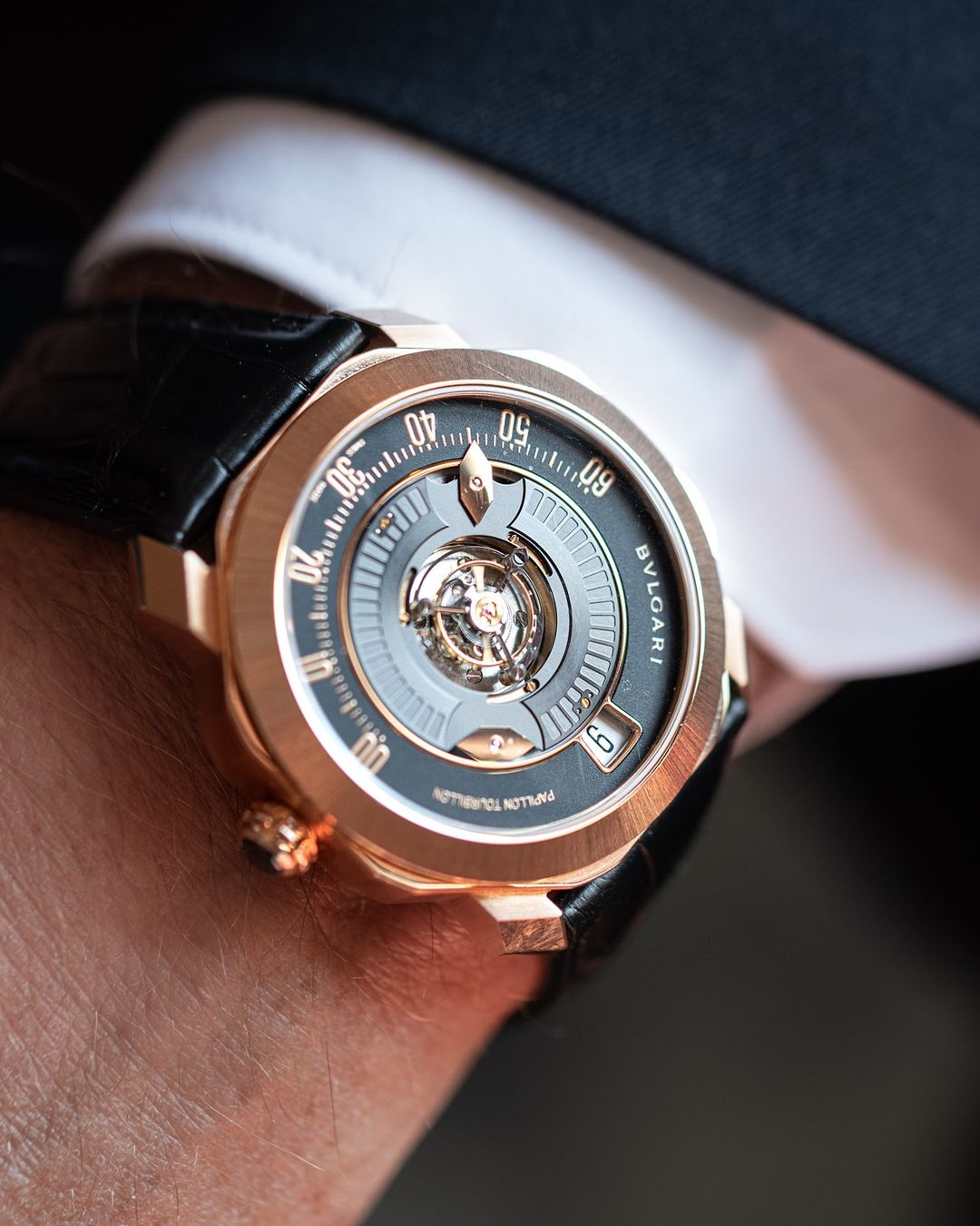 Close-up of a Bulgari watch featuring a black leather strap, gold casing, and skeleton dial, worn on a man's wrist with a crisp white cuff.