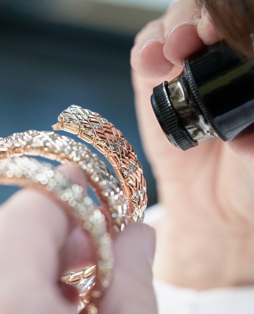 Close-up of a jeweller carefully examining a rose gold bracelet with diamonds using a magnifier. The jewelry is sparkling.