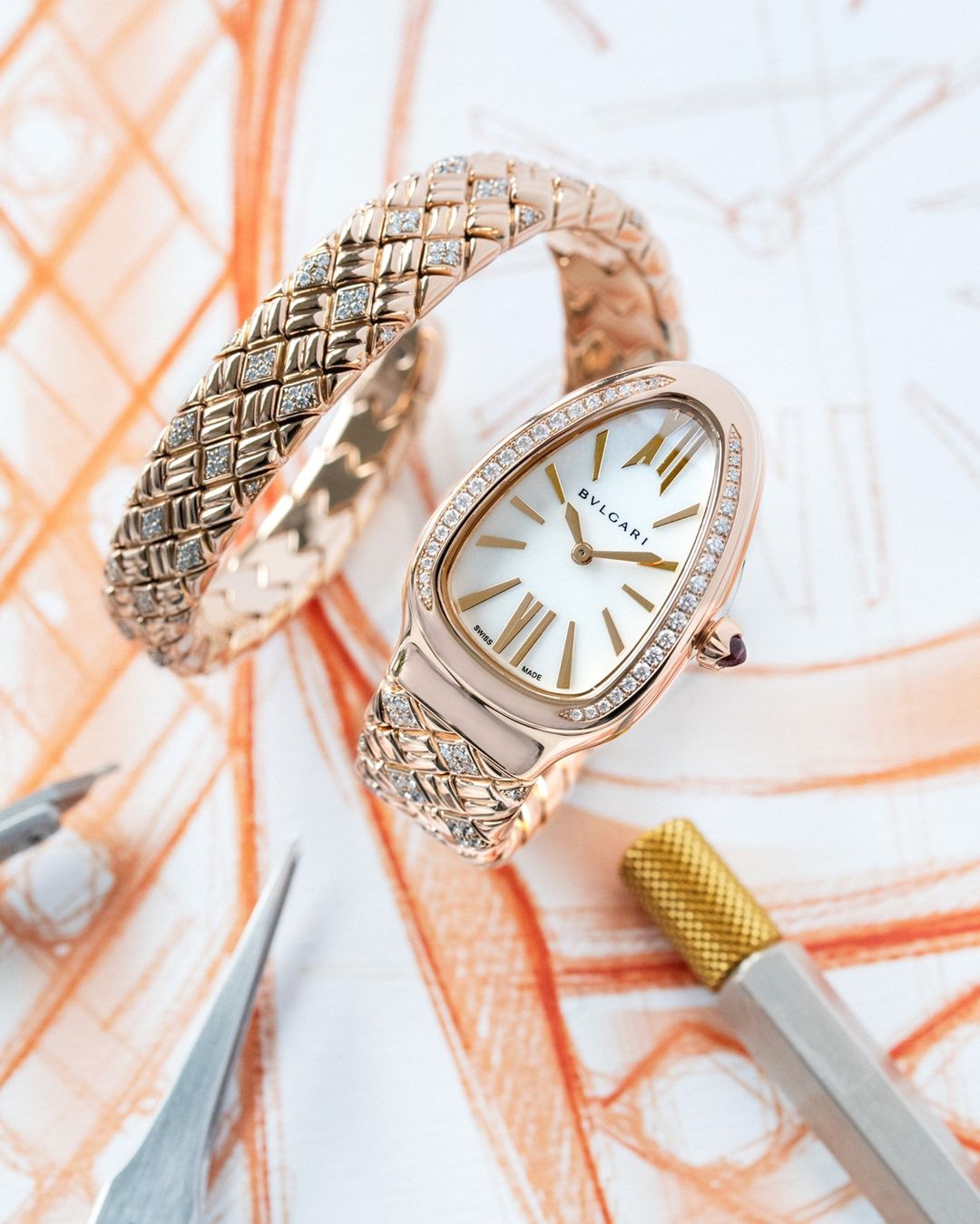 Elegant Bulgari watch and bangle set in rose gold with diamond accents, laid on a white surface with abstract orange sketching.