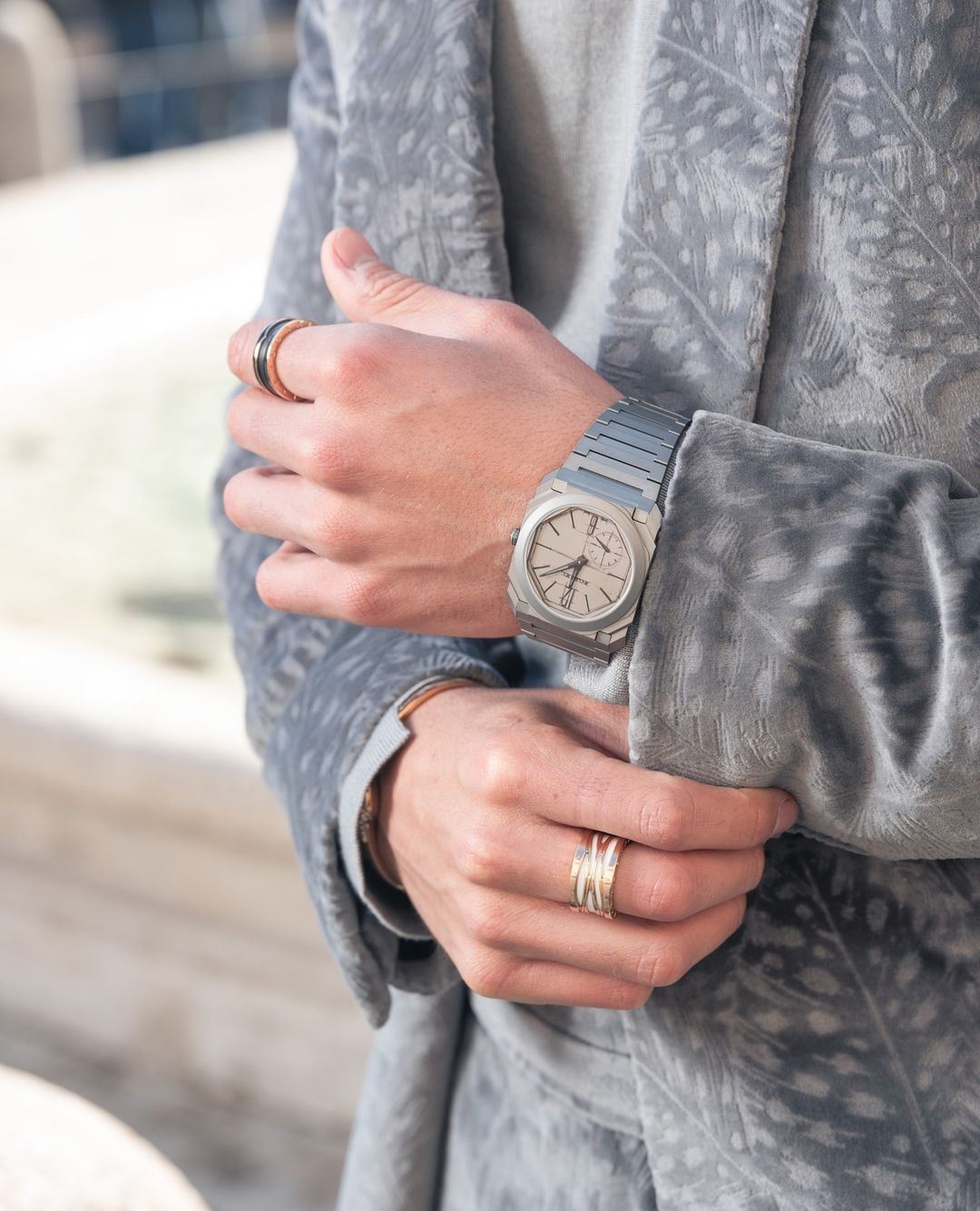 Close-up of a person's hands wearing a silver watch and rings, showcasing wrist accessories and stylish blazer.