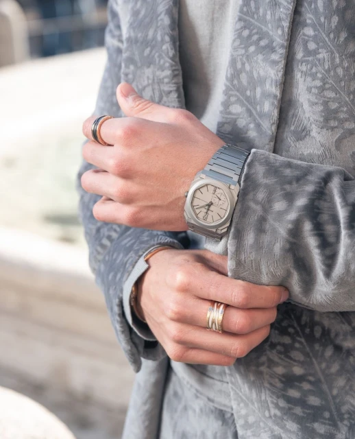 Close-up of a person's hands wearing a silver watch and rings, showcasing wrist accessories and stylish blazer.