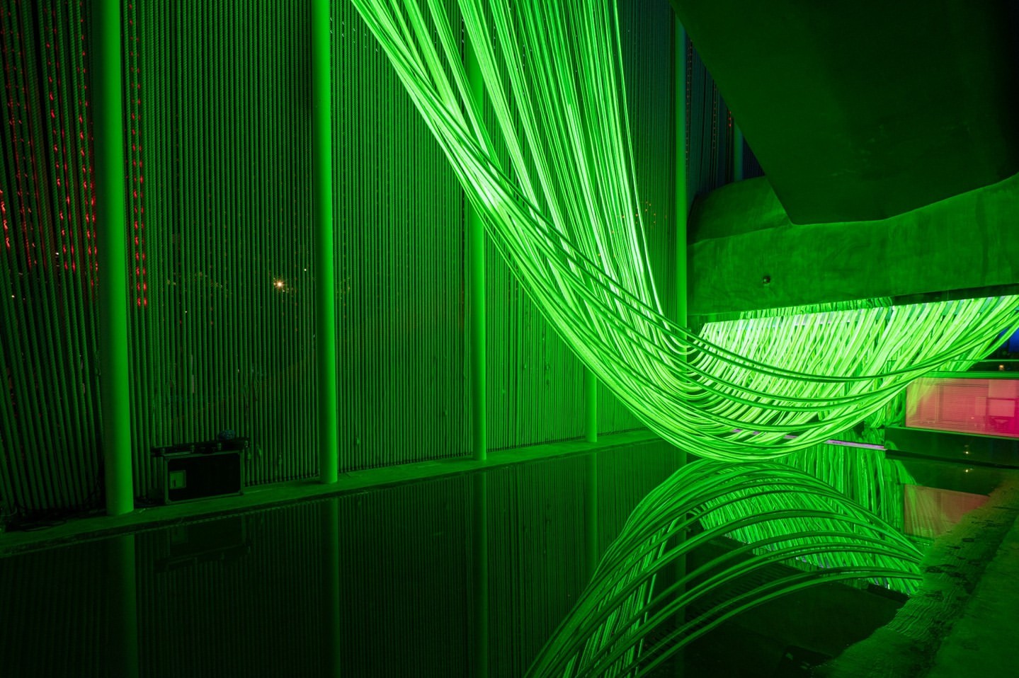 Abstract green light installation reflecting in water, creating a vibrant and immersive visual experience in an indoor setting.