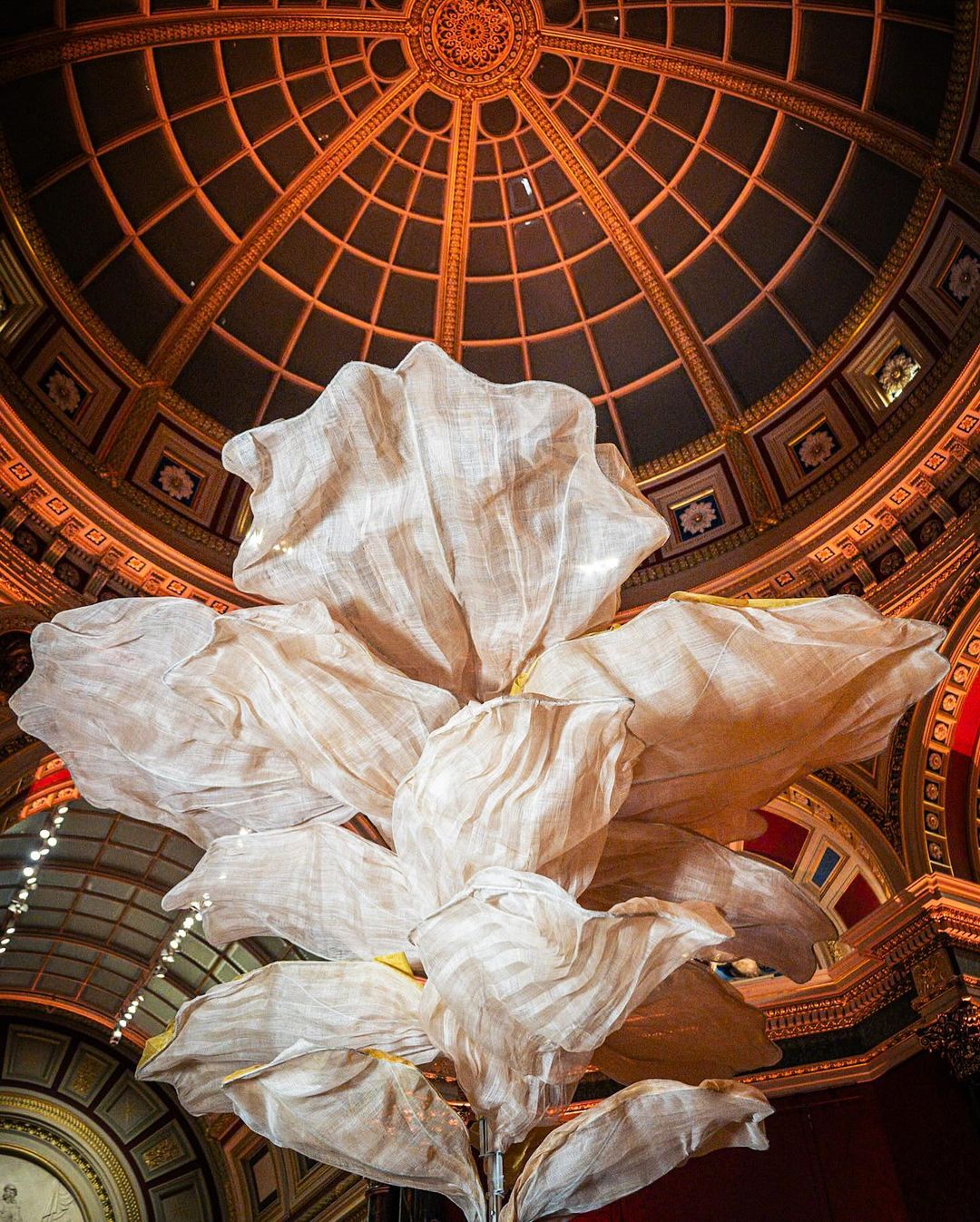 Interior shot of a large ornamental flower installation with white petals and a gilded dome ceiling in the backdrop, creating an artistic visual.