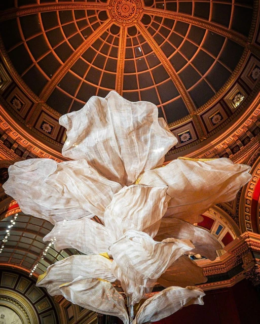Interior shot of a large ornamental flower installation with white petals and a gilded dome ceiling in the backdrop, creating an artistic visual.