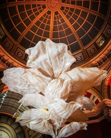 Interior shot of a large ornamental flower installation with white petals and a gilded dome ceiling in the backdrop, creating an artistic visual.