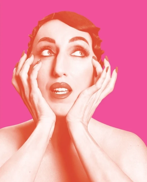Close-up portrait of an adult female with vintage hairstyle and vibrant pink lips, holding her hands up to her face with an open mouth expression.