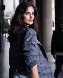 Woman with long dark hair wearing a grey plaid blazer looking back over her shoulder in Paris