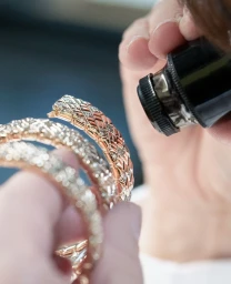 Close-up of a jeweller inspecting a rose gold diamond bracelet with a loupe in Paris by Gabriel De La Chapelle