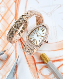 Rose gold Bvlgari watch and matching bracelet resting on an orange architectural sketch with drafting tools.