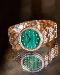 Rose gold diamond wristwatch with a green malachite face resting on a dark reflective surface in Paris by photographer Gabriel De La Chapelle