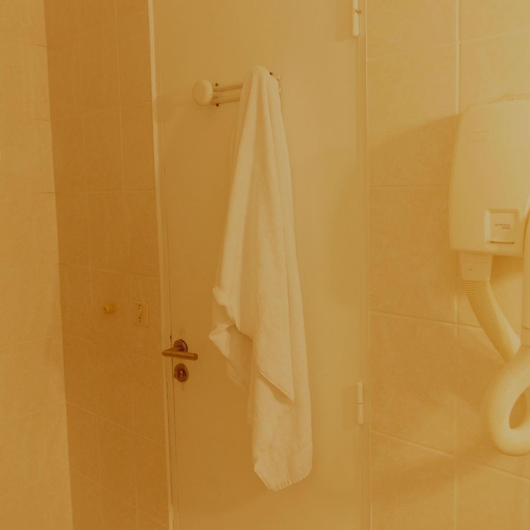 Bathroom interior features a white towel hanging on a rack, a wall-mounted hair dryer, a white door, and tiled walls in a yellow tone.