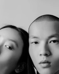 Close-up monochrome portrait of two models pressed close together against a plain light background by Gabriel Gomez in Paris.