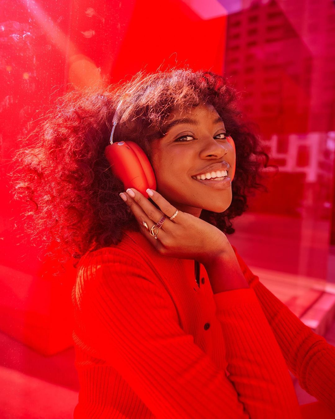 Portrait of a smiling African-American woman wearing red headphones and a matching red top in an indoor setting with a red backdrop.