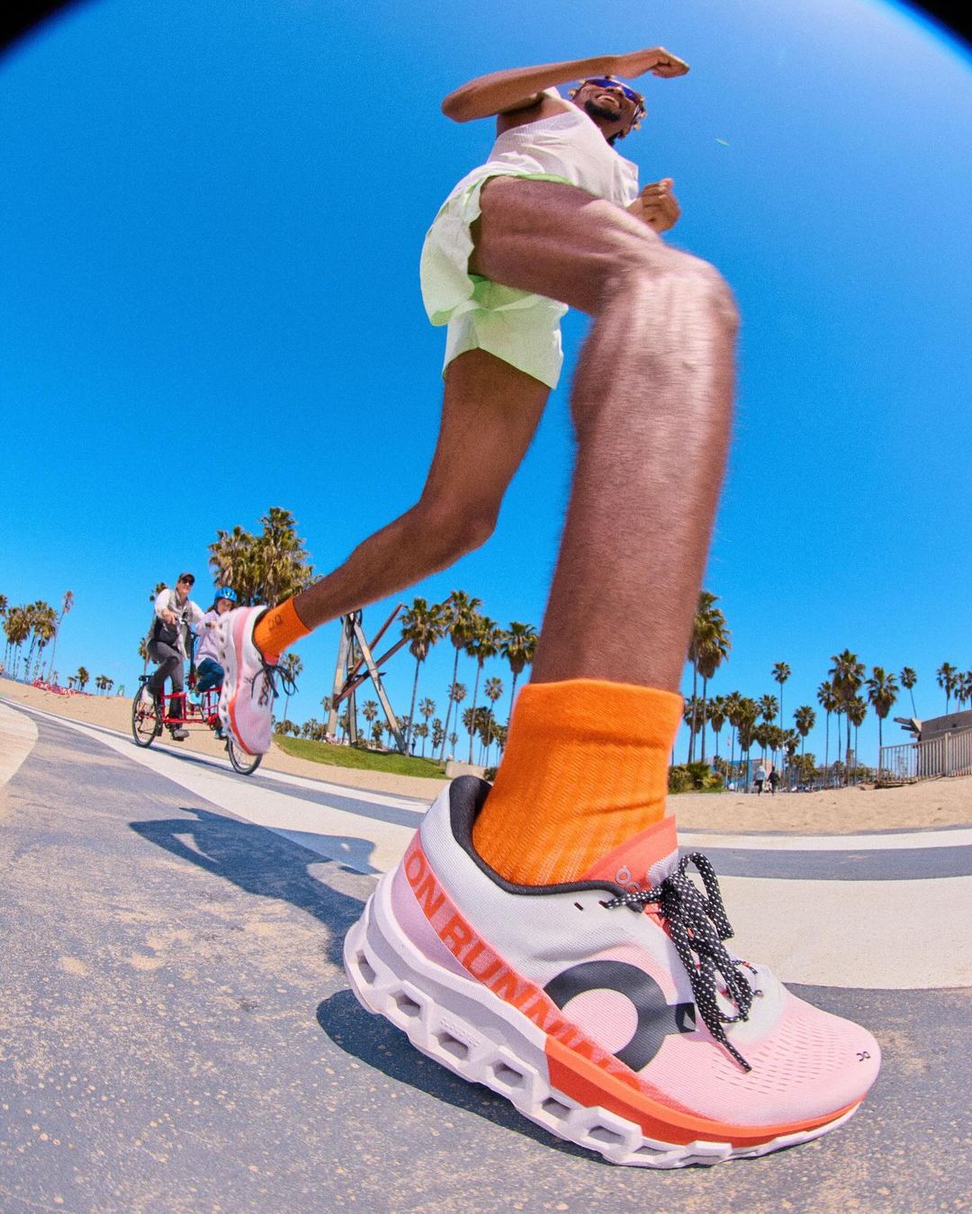 Close-up of running shoe on a man running outdoors on a sunny day near palm trees; low angle, wide shot, vibrant colors.