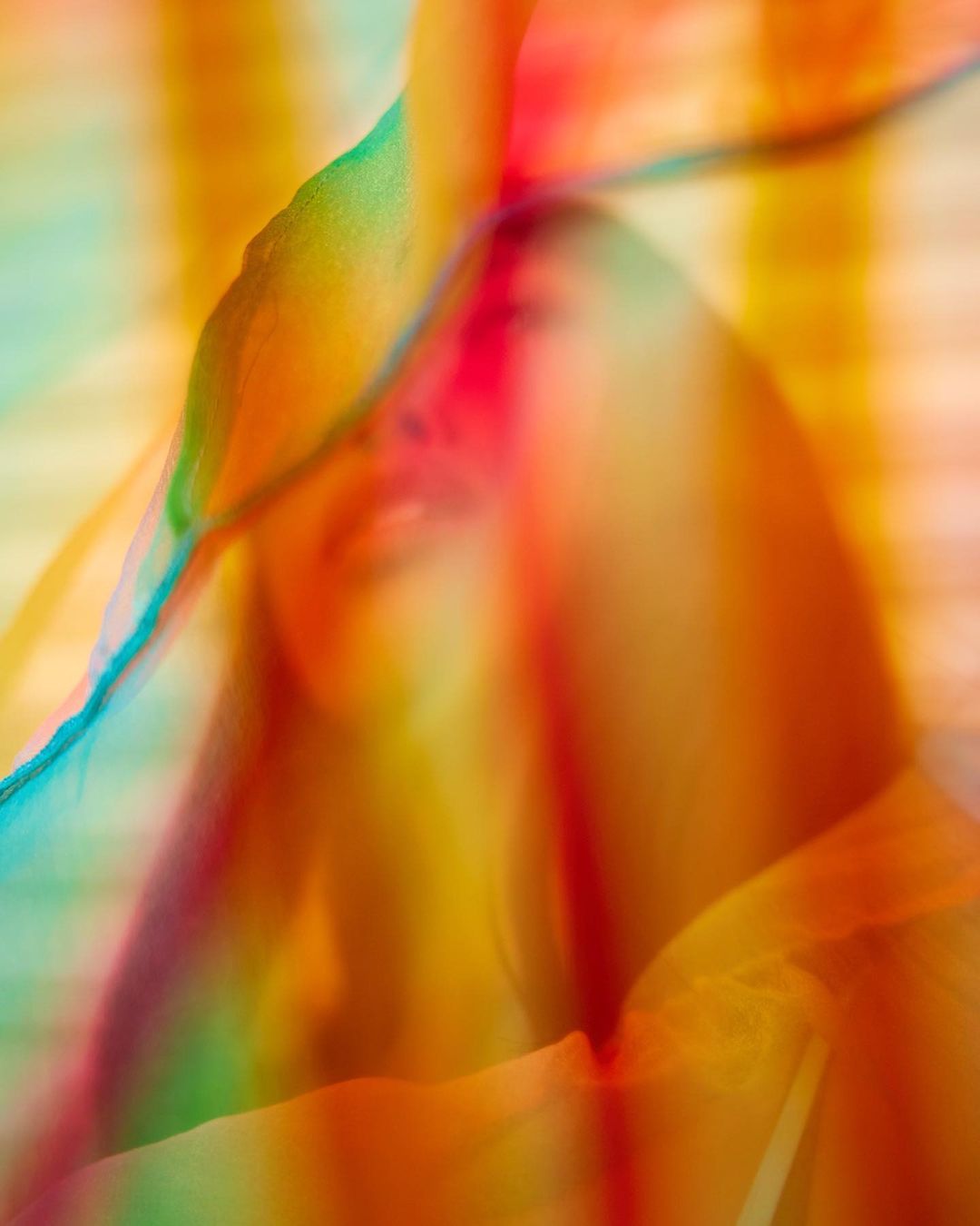 Woman's face obscured by colorful flowing fabric in a blurry, dreamlike image with a vibrant and abstract aesthetic.