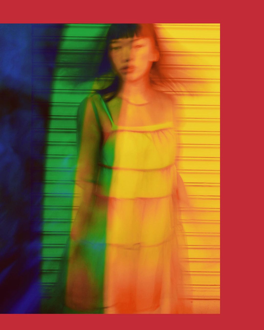 Abstract fashion portrait of an Asian woman with dark hair wearing a yellow dress standing in front of a colorful wall.