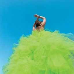 Model in a voluminous bright green tulle gown with hands raised against a clear blue sky