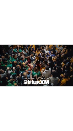 Large crowd of people celebrating with drinks at a basketball game, many wearing green, with the SiriusXM logo in the foreground.