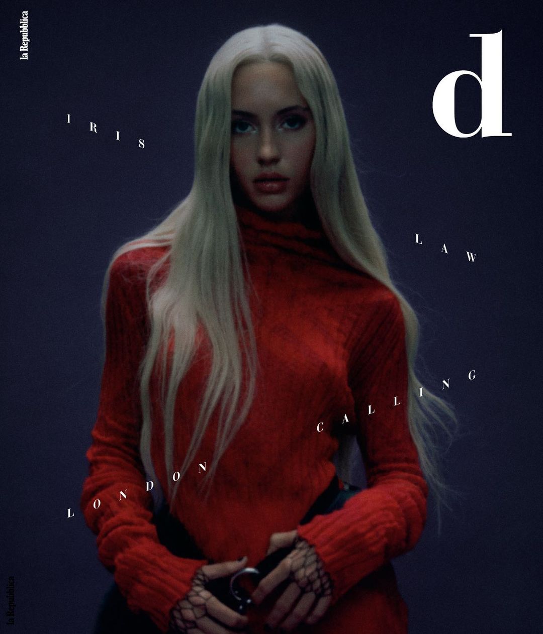 Magazine cover featuring a fair-skinned woman with blonde hair wearing a red turtleneck sweater against a dark background.