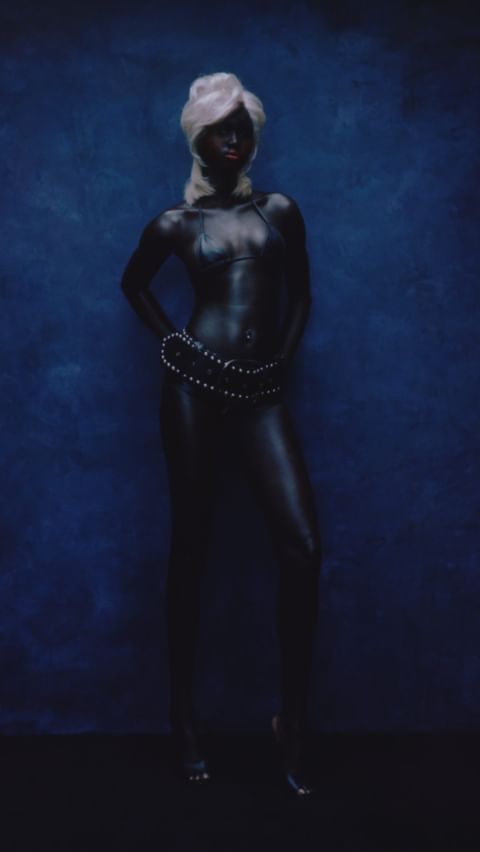 Artistic studio portrait of an African-American female model with an updo, body paint, and beaded jewelry against a blue backdrop.
