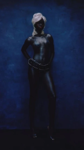 Artistic studio portrait of an African-American female model with an updo, body paint, and beaded jewelry against a blue backdrop.